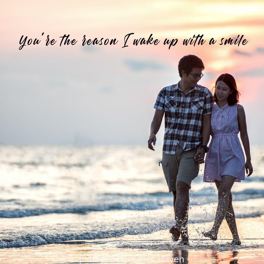 You're the reason I wake up with a smile. A boy and girl walking hand in hand on the sea shore on the sand with visible foot steps. relationship and love. romantic couple images and quotes. Love Quotes and Images for Couples. HD images. Free download.